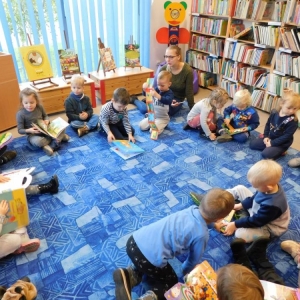 Dzieci siedzą na dywanie w kółeczku i oglądają książki